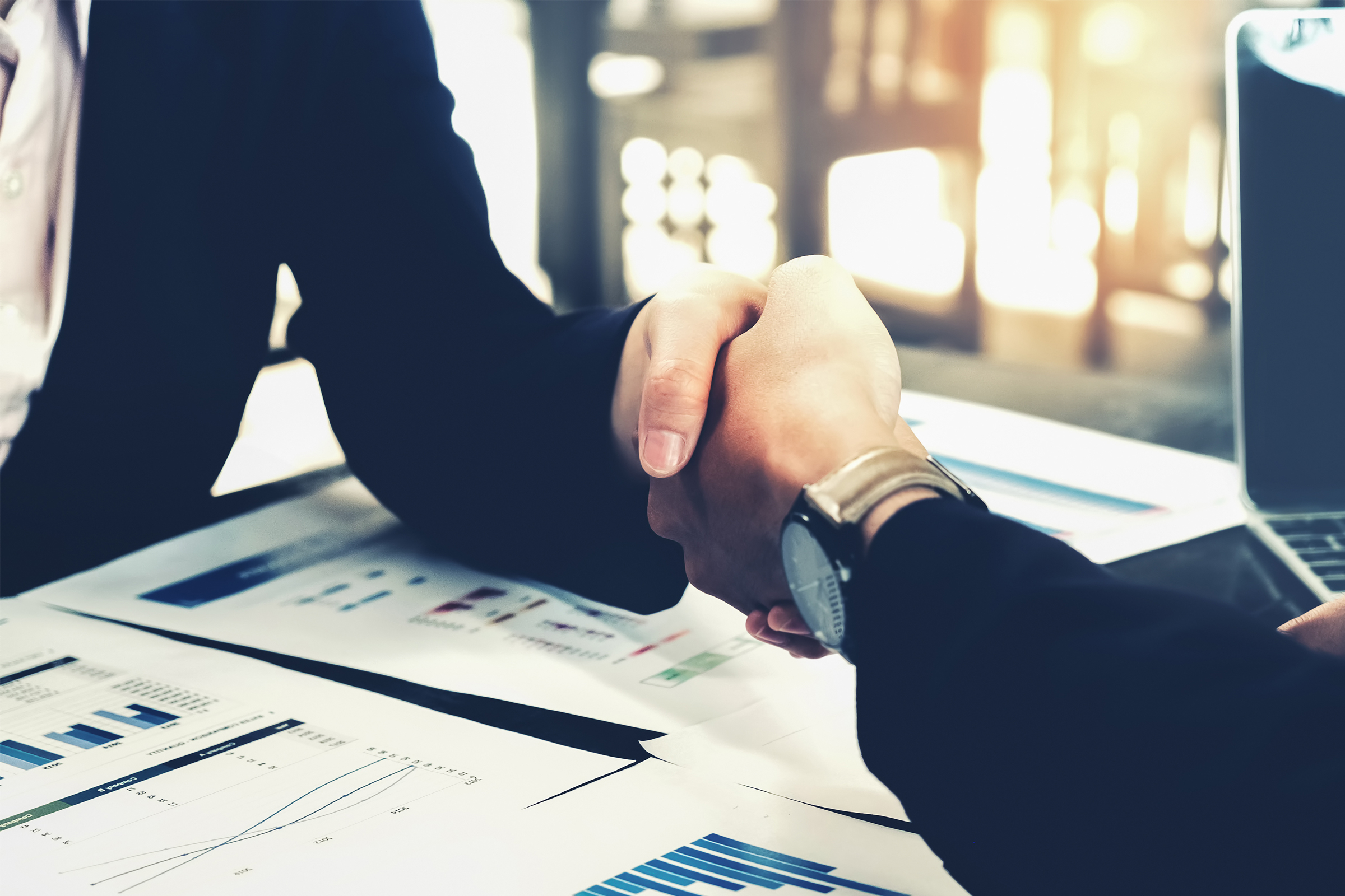 Kaksi kättä kättelee asiakirjoja sisältävän pöydän yli.