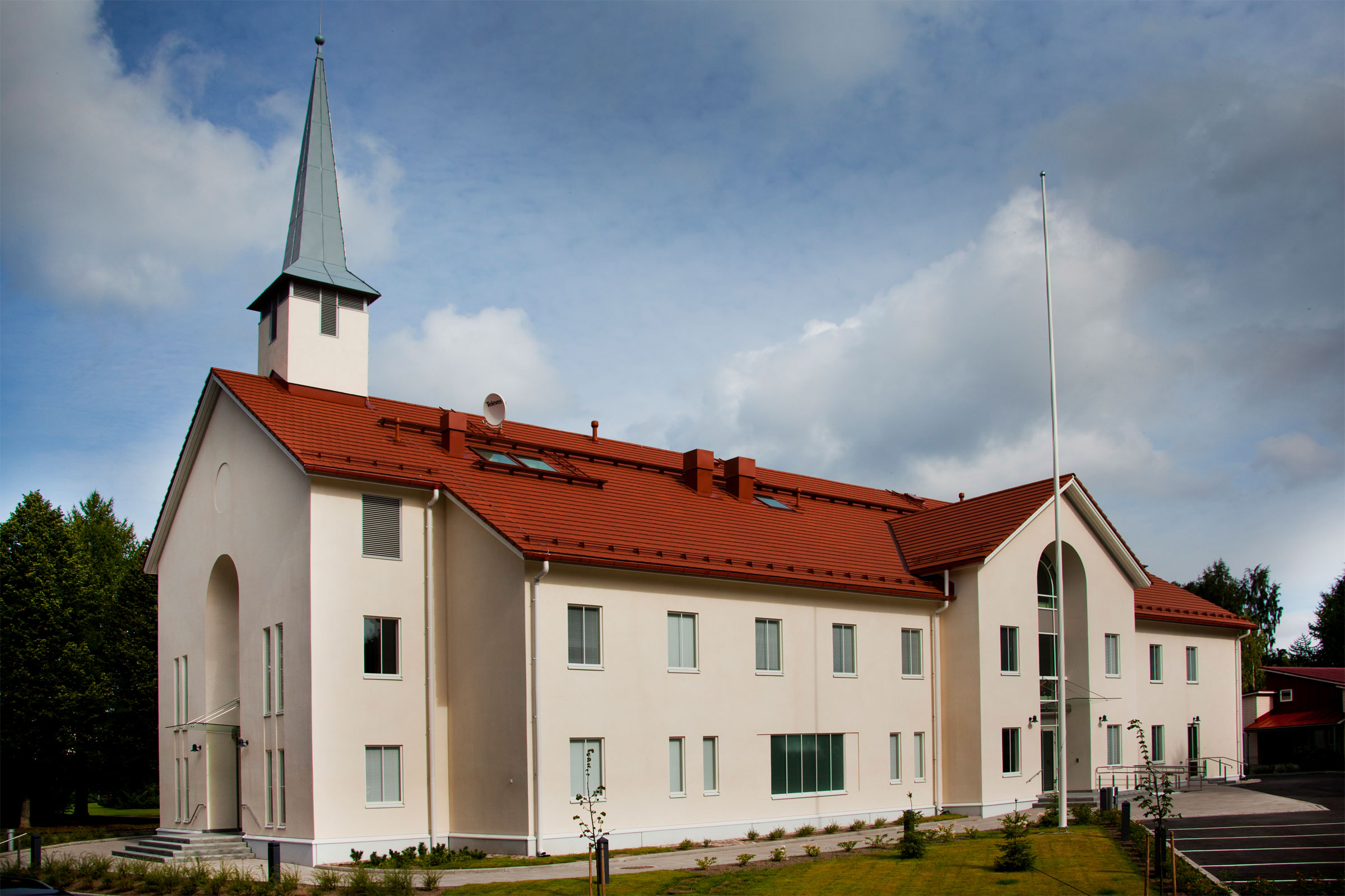 Valkoinen suorakaitee mallinen kolmikerroksinen kirkko tiilenpunaisella katolla, suippo kirkontorni