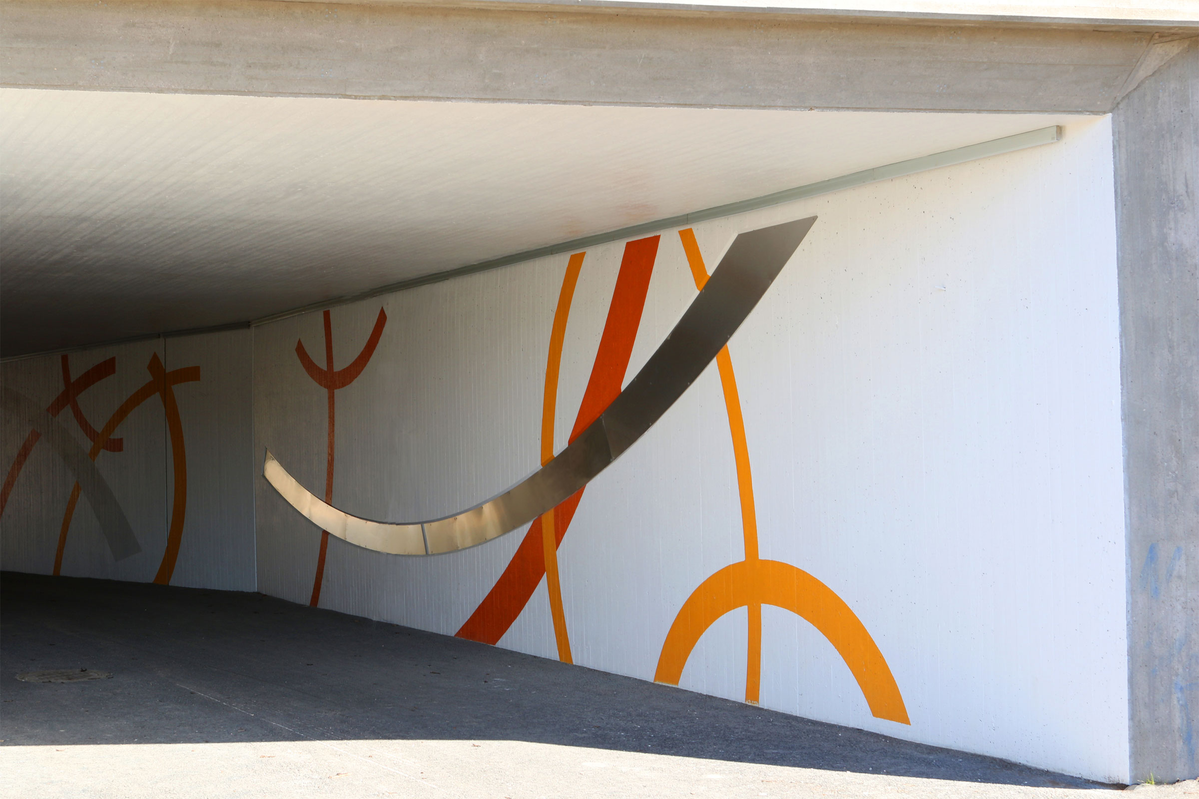 Valkoinen alikulkutunneli punaiset, oranssiset ja kullanväriset kaarikuviot.