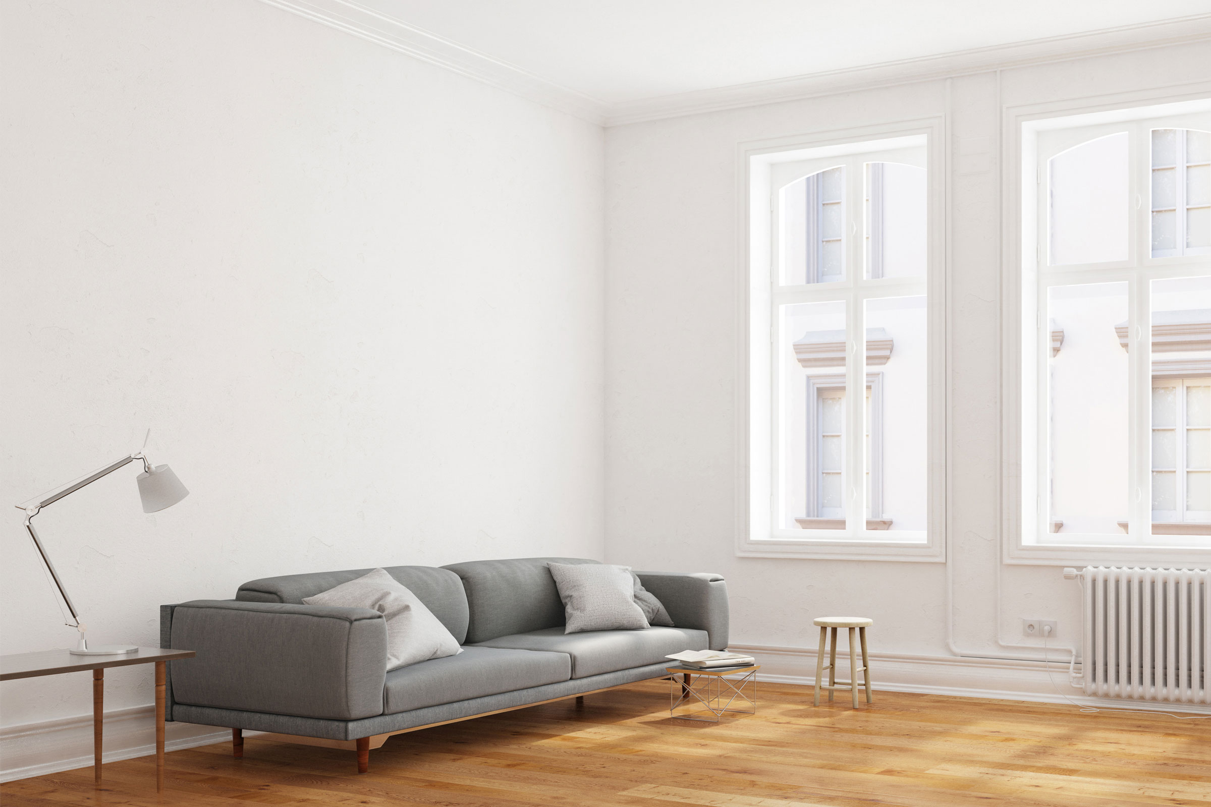 Kerrostalon ikkunallinen olohuone, jossa valkoiset seinä, harmaa sohva ja puulattia.