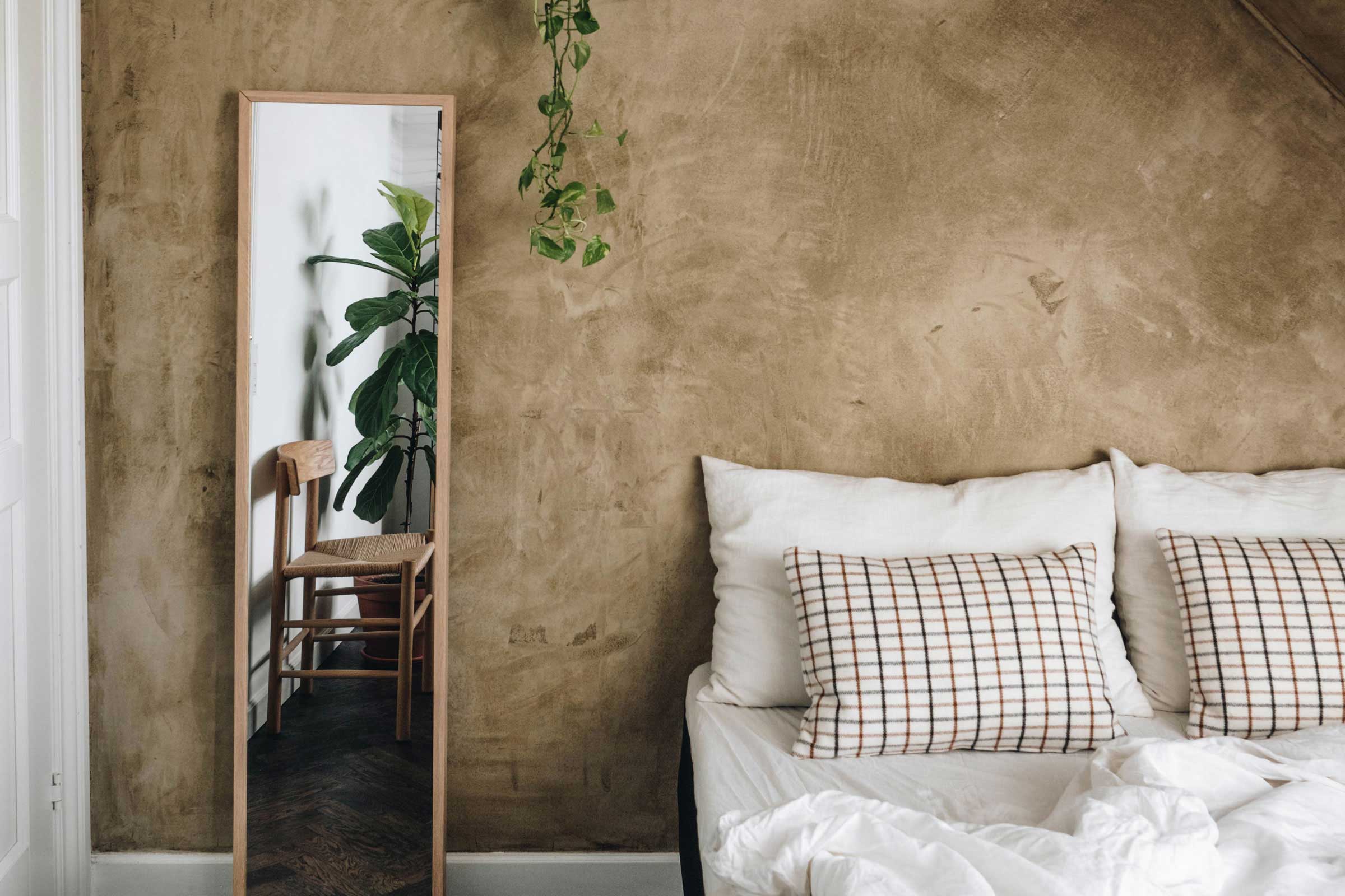 Makuuhuone, jossa on beige kalkkiseinät, peili seinällä ja sänky valkoisilla liinavaatteilla.