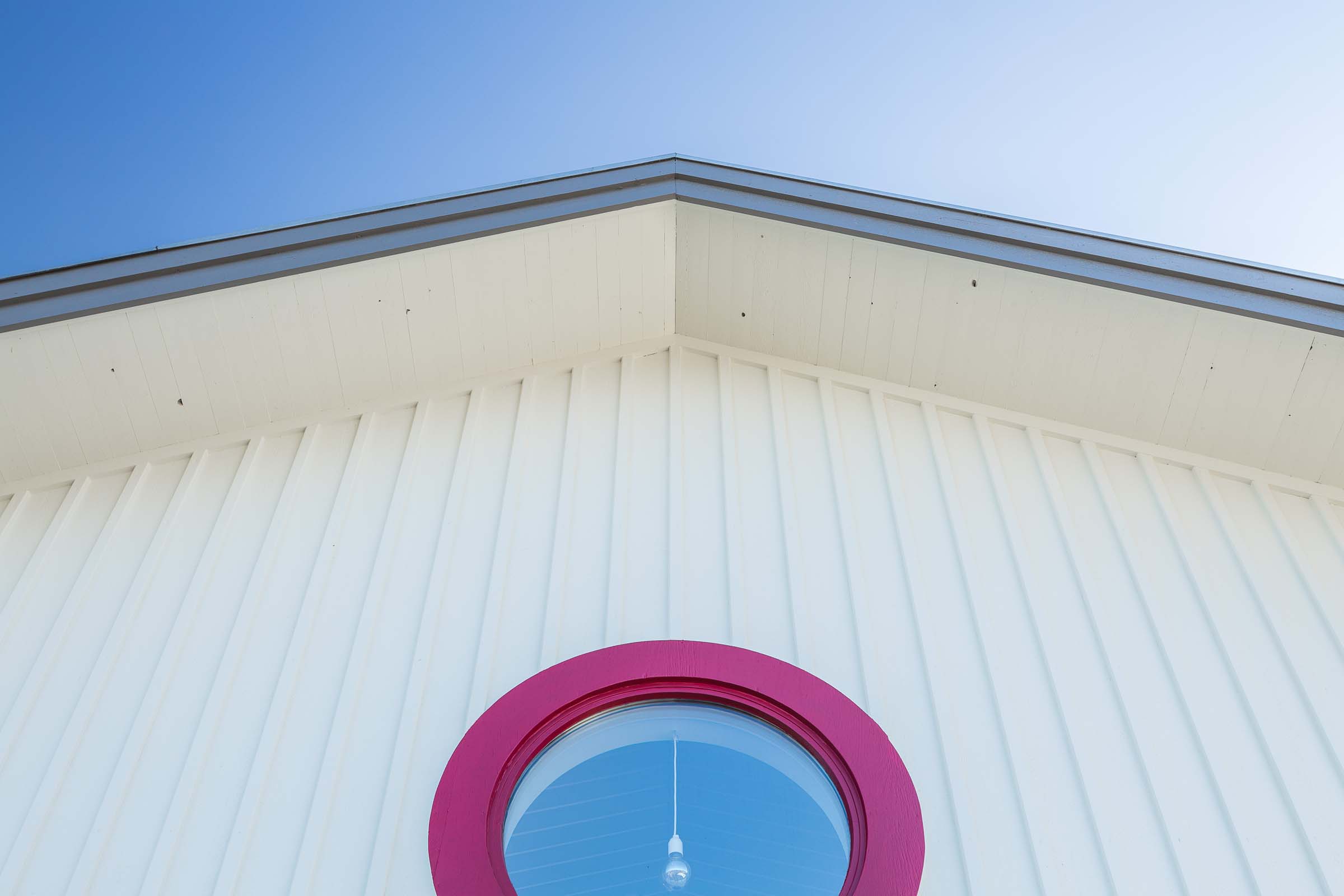 Vit träfasad. Runt fönster med rödmålad fönsterkarm.