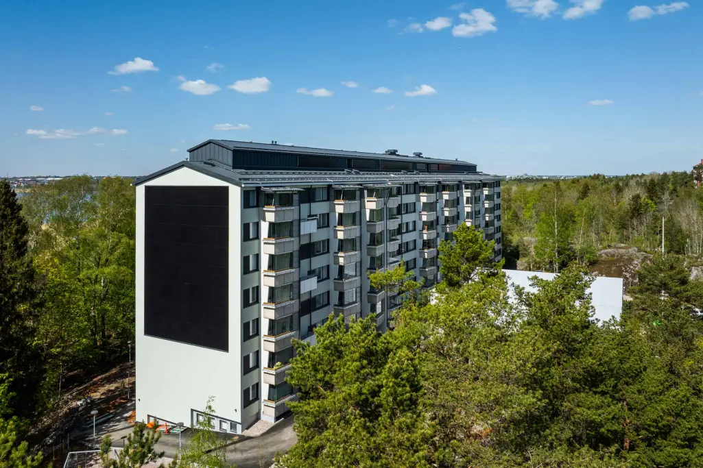 Levyrapattu kerrostalo, jonka päädyssä on isona yhtenäisenä elementtinä aurinkopaneeleita.
