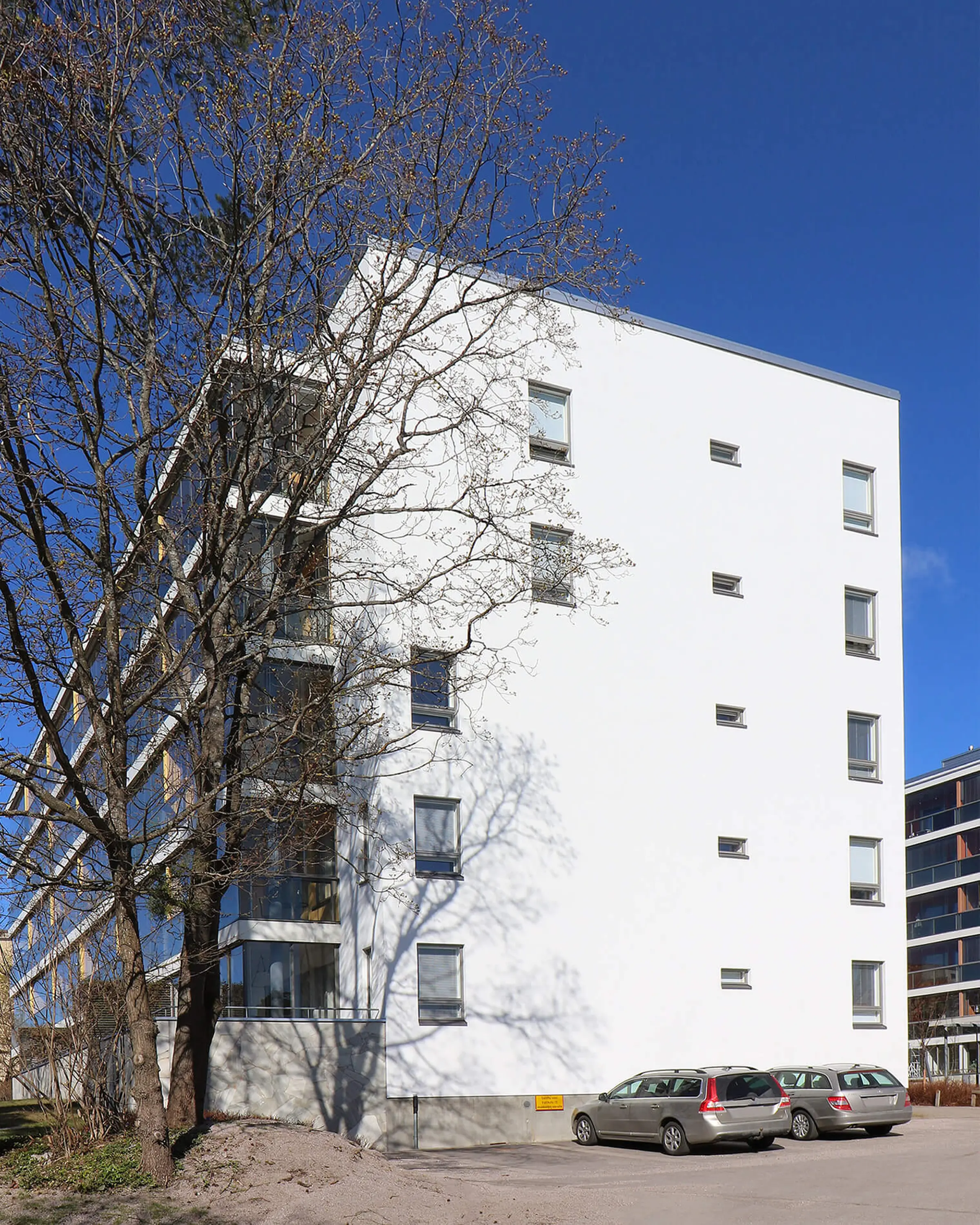 Valkoisen kerrostalon pääty. Päätyseinässä on ikkunoita ja toisella sivulla näkyy parvekkeet.