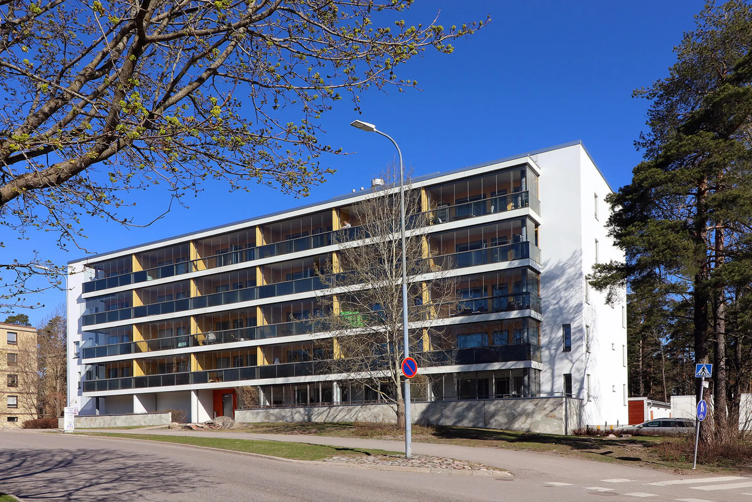 Valkoiseksi rapattu neljäkerroksinen kerrostalo lasitetuilla parvekkeilla.