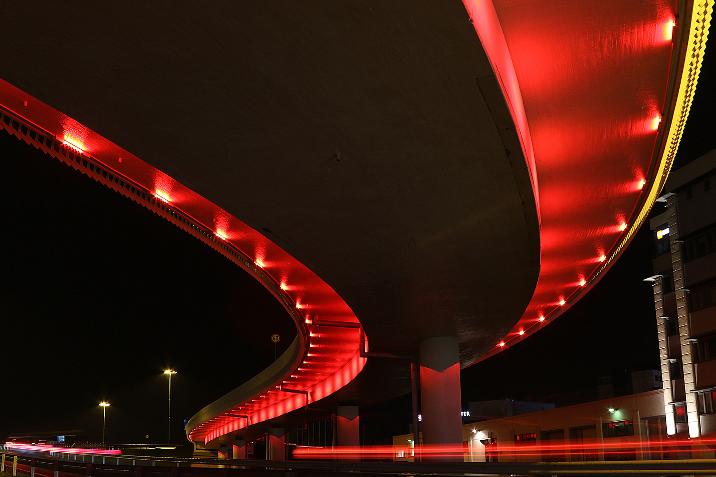 Punaiseksi valaistu silta kuvattuna alhaalta päin.