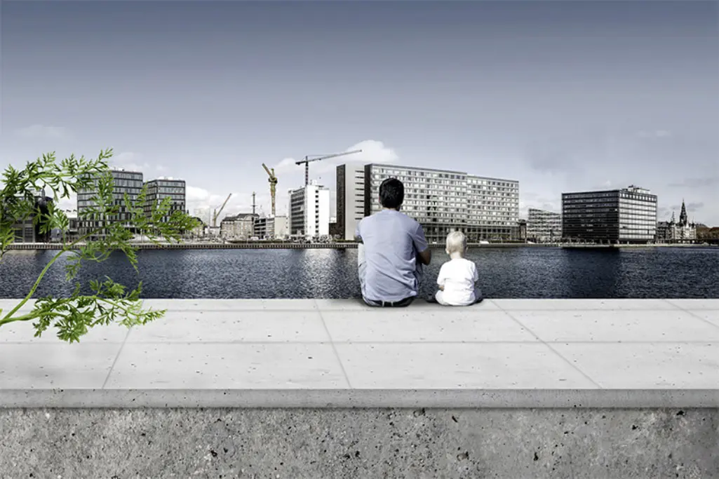 Mies ja lapsi istuvat katsellen vastarannalla avautuvaa kaupunkimaisemaa.